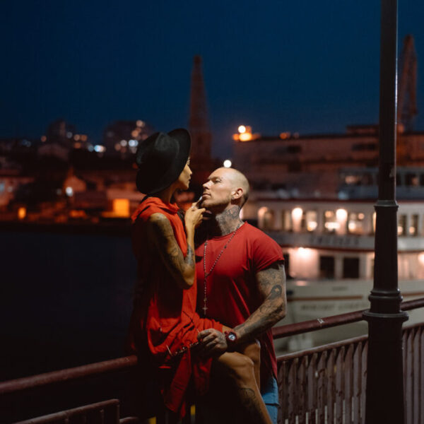 The young, modern, couple of lovers pose for a camera on the night promenade. The port is in the background